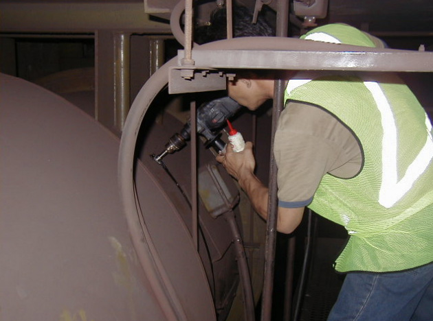 A man in a high-vis vest drilling an access hole for conduit into a machine