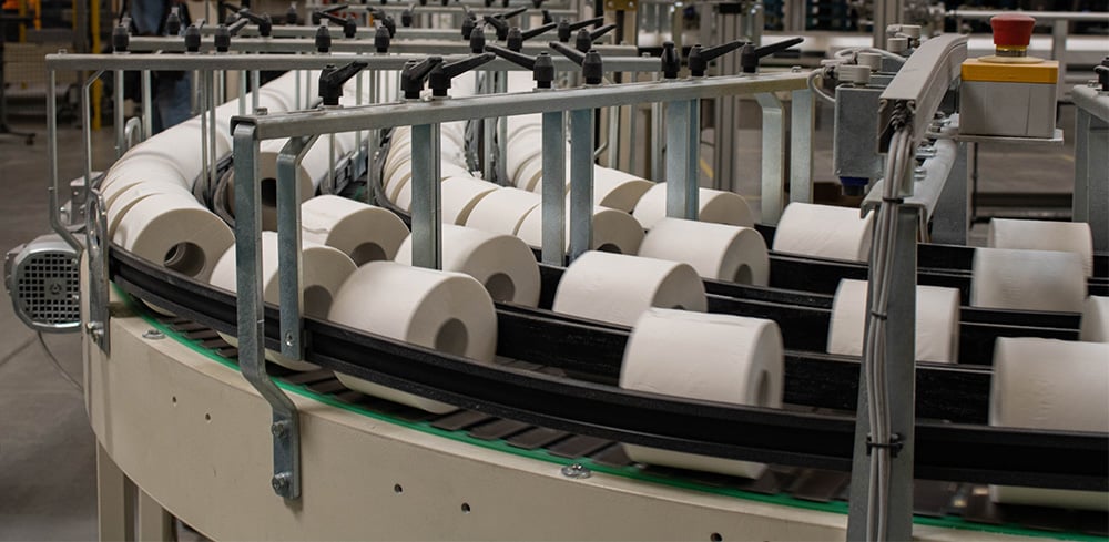 White rolls of toilet paper moving on an industrial metal conveyor belt inside a paper production factory
