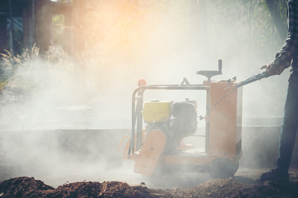 Man using industrial concrete saw in cloud of dust.
